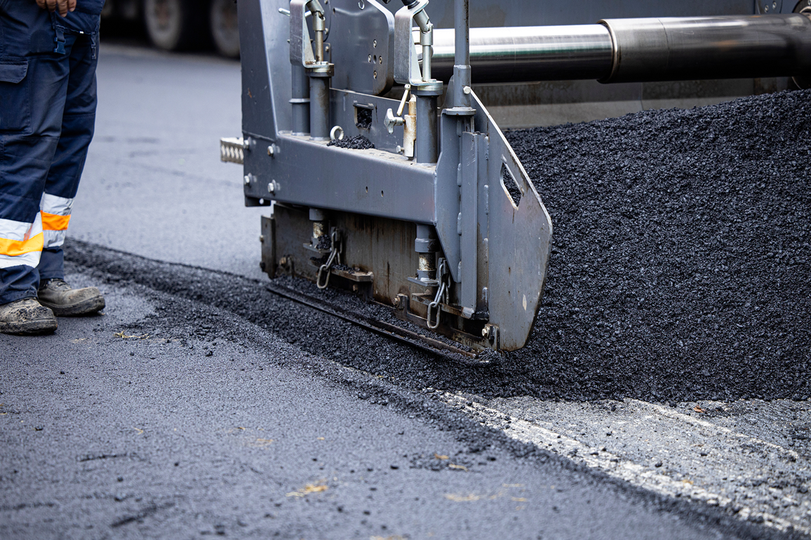 Closeup of machine and worker applying asphalt layer to parking lot